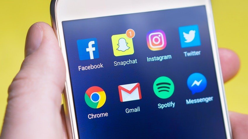 fotografia de um celular na mão, na tela há ícones das principais redes sociais